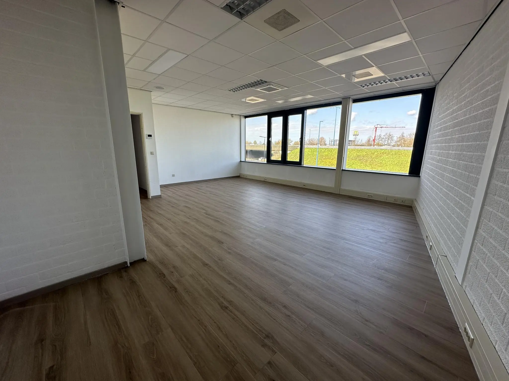 Lichte, lege kantoorruimte aan de Van Der Hagenstraat met grote ramen en houten vloer.